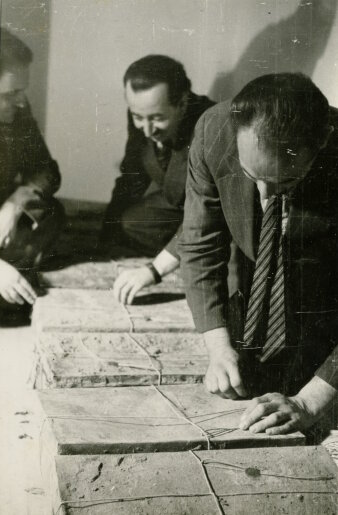 schwarzweiß Foto von drei Männern die alte Unterlagen öffnen