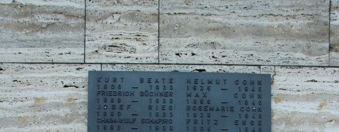 Ehrenhain Schapiro Ausschnitt einer Metalltafel auf einer Steinwand. Darauf stehen Namen und Lebensdaten
